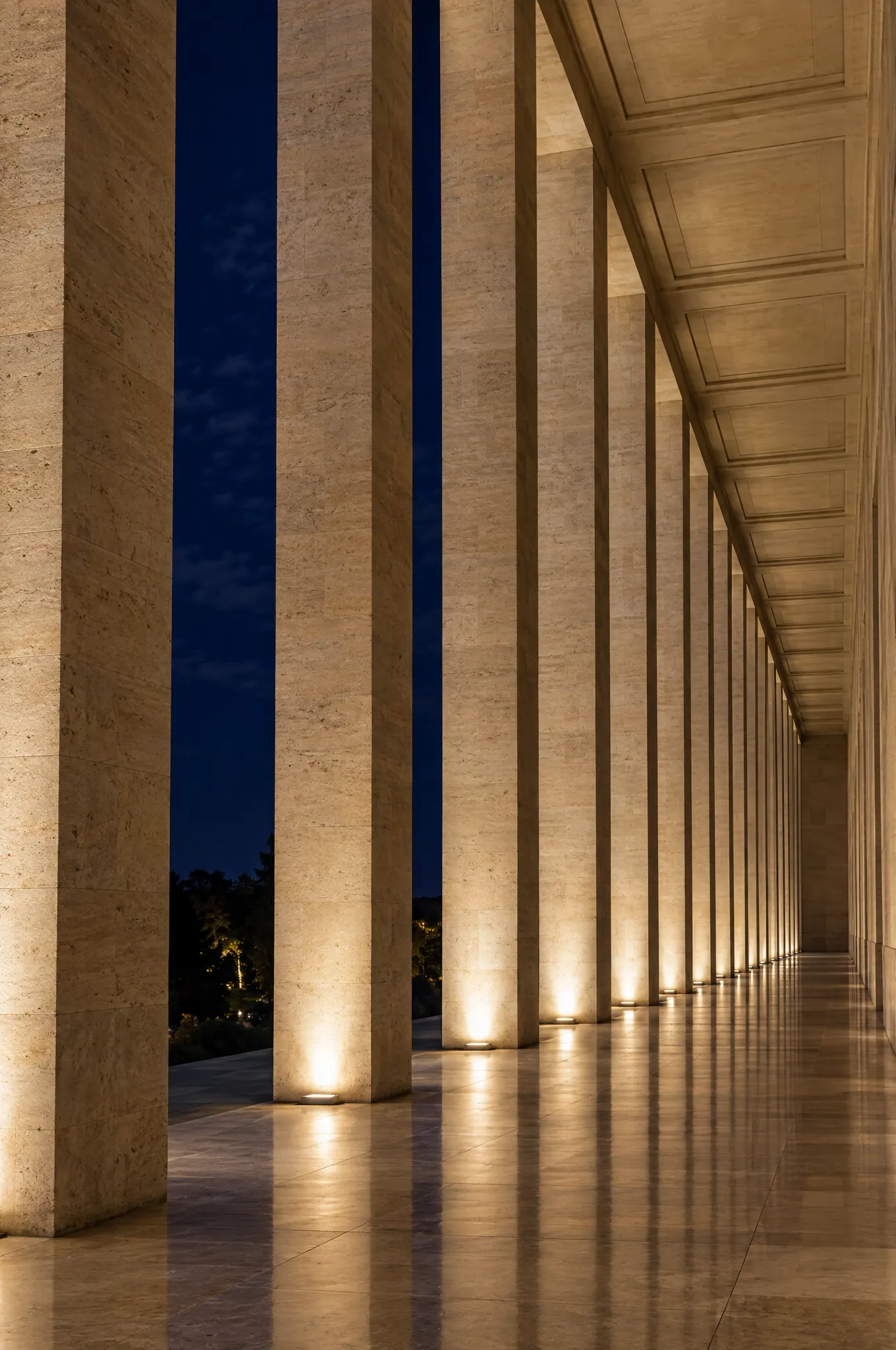 A long limestone colonnade at night, softly lit from below